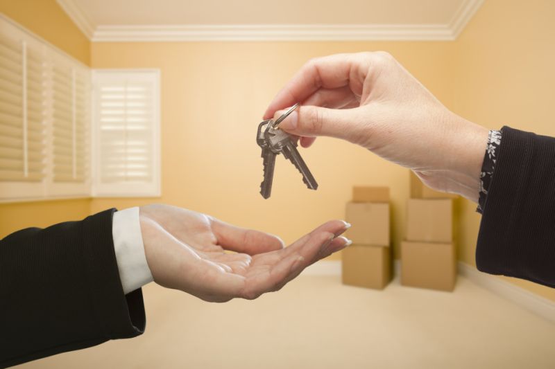 Woman Handing Over the House Keys To A New Home Inside Empty Room.