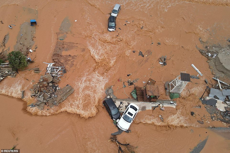 Debris and damaged cars can be seen on the flooded coastal road.