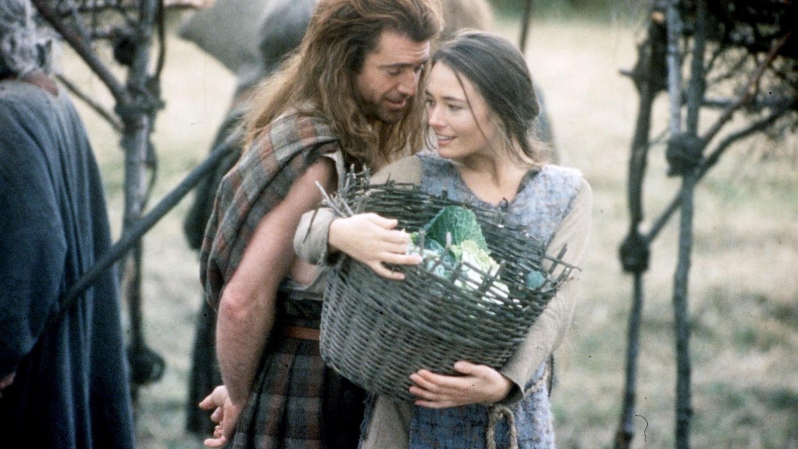 A man wearing a plaid behind a woman carrying a basket (Mel Gibson).