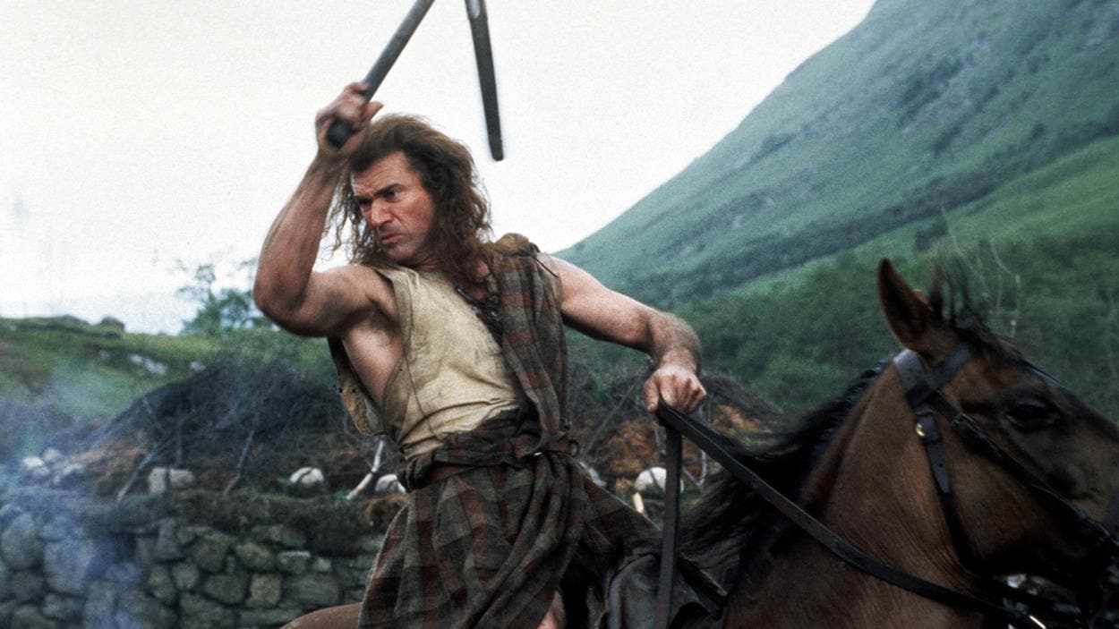 A man (Mel Gibson) with weapons and tartan, on horseback, ready for battle.