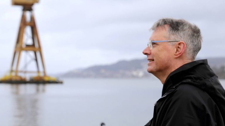 Roar Iversen, mann med briller i profiil, ser utover vann i Bergen, gul kran i bakgrunnen.