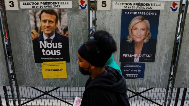 People walk in front of the campaign posters of Emmanuel Macron and Penn in Marine